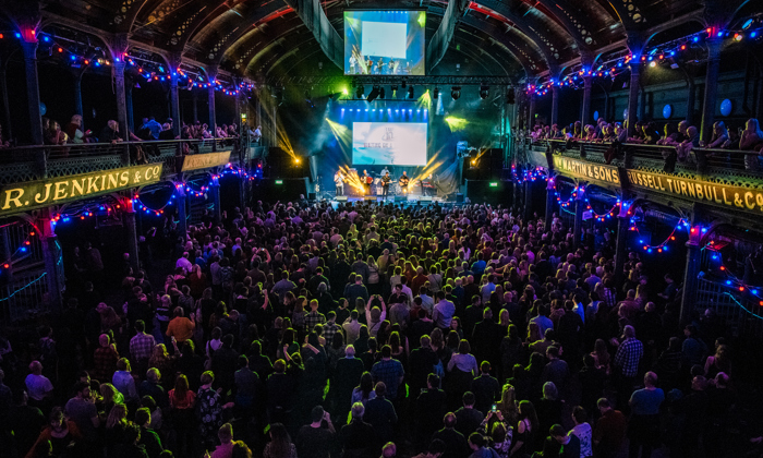 Band playing on stage at Old Fruitmarket with full audience watching 