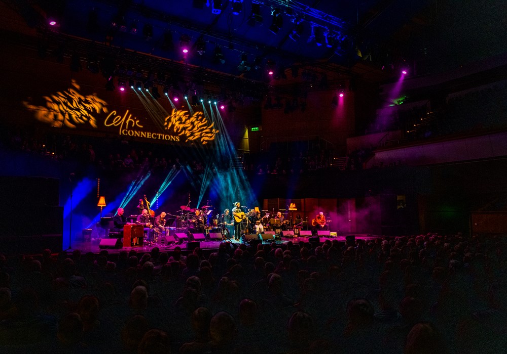 Musicians on a stage with multicoloured stage lights. The words Celtic Connections are displayed in the concert hall.